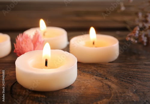 Burning candles and flower on wooden table, closeup