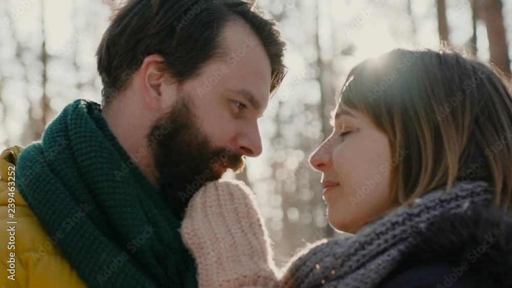 A young guy and a girl dressed in warm winter clothes, enjoy the presence of each other in a snowy winter park. closeup kiss. 4k slow motion. A young guy and a girl dressed in warm winter clothes, enjoy the presence of each other in a snowy winter park. closeup kiss. 4k slow motion.