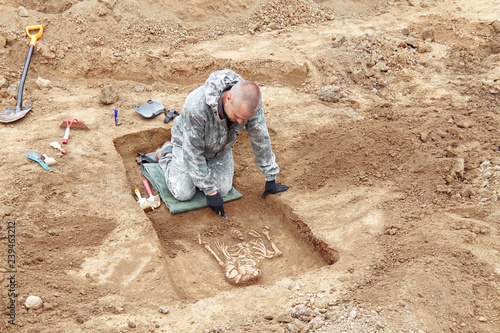 Archaeological excavation. The archaeologist in a digger process, searching tomb with tools, human bones, part of skeleton and skull in the ground. Close up, outdoors.