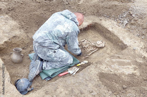 Archaeological excavation. The archaeologist in a digger process. searching the tomb, hands with tools, human bones, part of skeleton and skull in the ground. Close up, outdoors.
