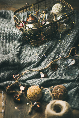 Christmas, New Year holiday festive mood. Grey woolen sweater, led garland and vintage Christrmas decoration toys in box over wooden rustic table background, close-up, vertical composition photo