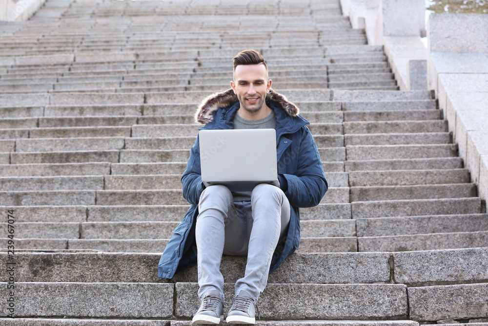 Young man with laptop sitting on stairs outdoors