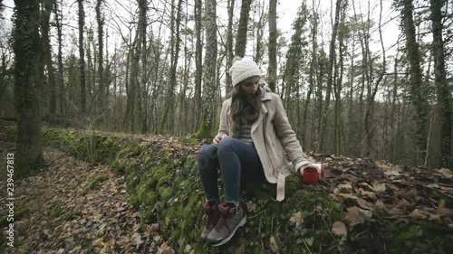 Girl sitting on a stone wall from a german fortification building during the second Reich and drinking herbal infusion from thermos. photo