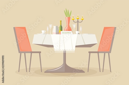 Reserved restaurant or cafe table with tablecloth, candles in candlestick, plant, wineglasses, reservation tabletop sign on it and two chairs