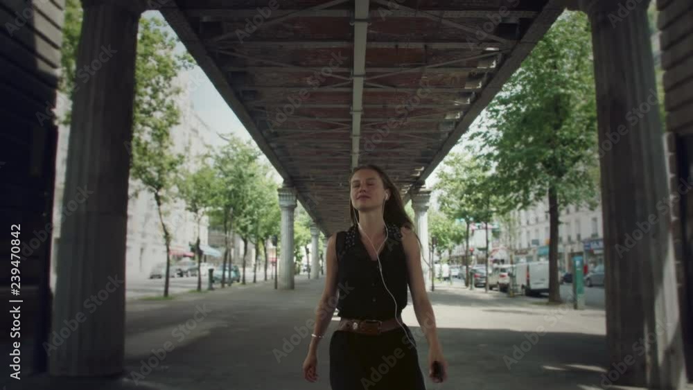 Portrait of a stunning confident woman walking underneath a bridge in France tuned in to her music, she walks toward the camera and laughs when she opens her eyes Portrait of a stunning confident woman walking underneath a bridge in France tuned in to her music, she walks toward the camera and laughs when she opens her eyes