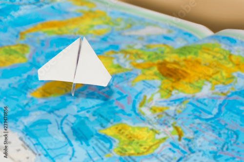 small paper airplane over a geographical map of the world. selective focus. Concept: air travel, cargo delivery, travel, international messages, mail.