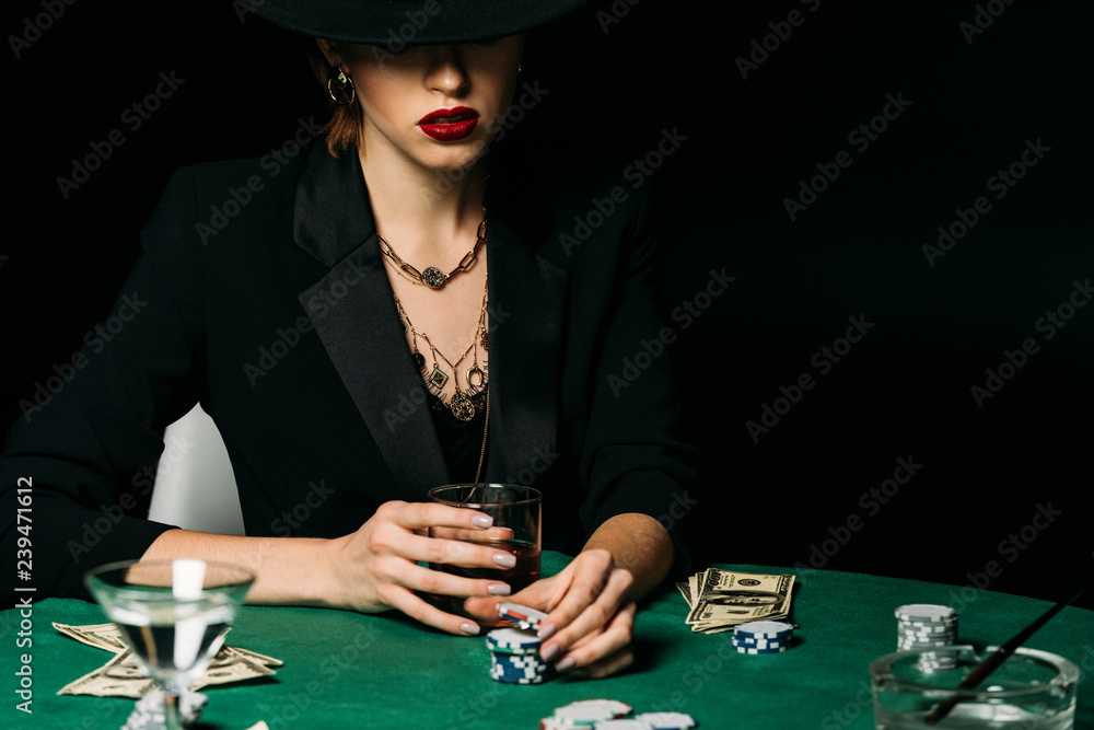 attractive girl in jacket and hat holding glass of whiskey and taking poker chip in casino attractive girl in jacket and hat holding glass of whiskey and taking poker chip in casino