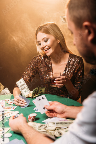 happy beautiful girl playing poker with croupier at casino  dollar banknotes falling on table