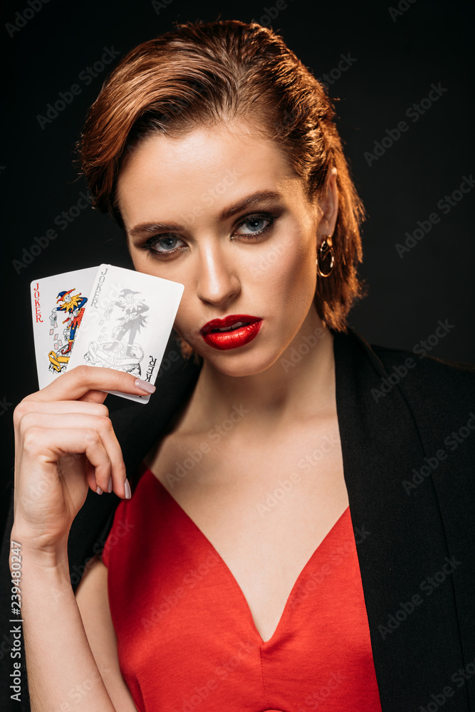 portrait of attractive girl in red dress and black jacket holding poker cards and looking at camera isolated on black portrait of attractive girl in red dress and black jacket holding poker cards and looking at camera isolated on black