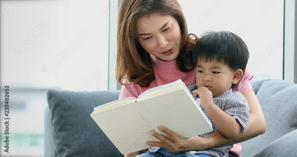 Asian mother and her son sitting on sofa together, their reading some book, sharing their happy time, concept for mother and son. Asian mother and her son sitting on sofa together, their reading some book, sharing their happy time, concept for mother and son.