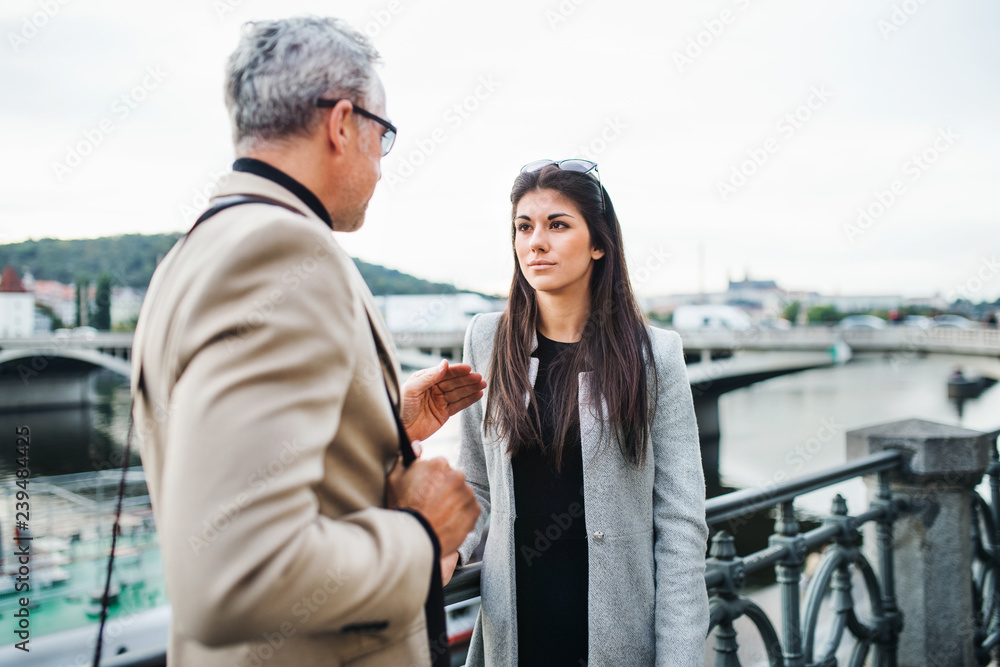 Man and woman business partners walking by a river in city of Prague, talking. Man and woman business partners walking by a river in city of Prague, talking.