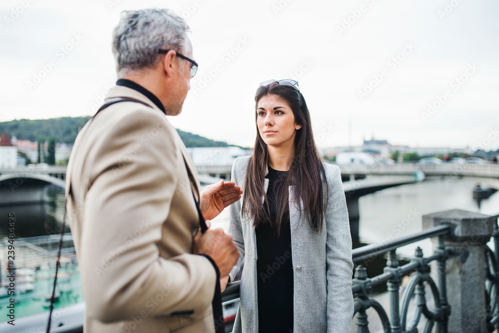 Man and woman business partners walking by a river in city of Prague, talking.