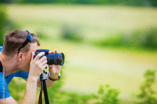 Professional photographer checks the camera settings, looking into the viewfinder against the background of mountains and slopes