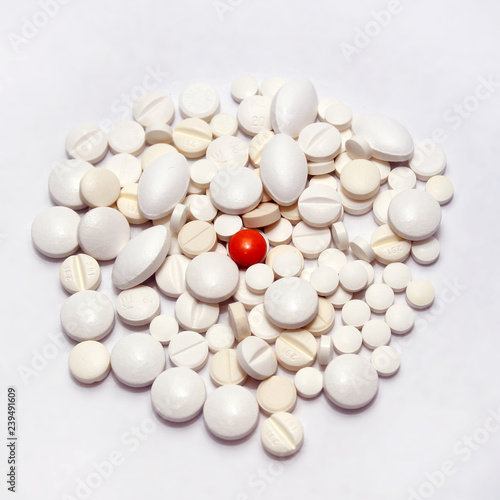 A scattering of different white pills on a white background, one orange pill