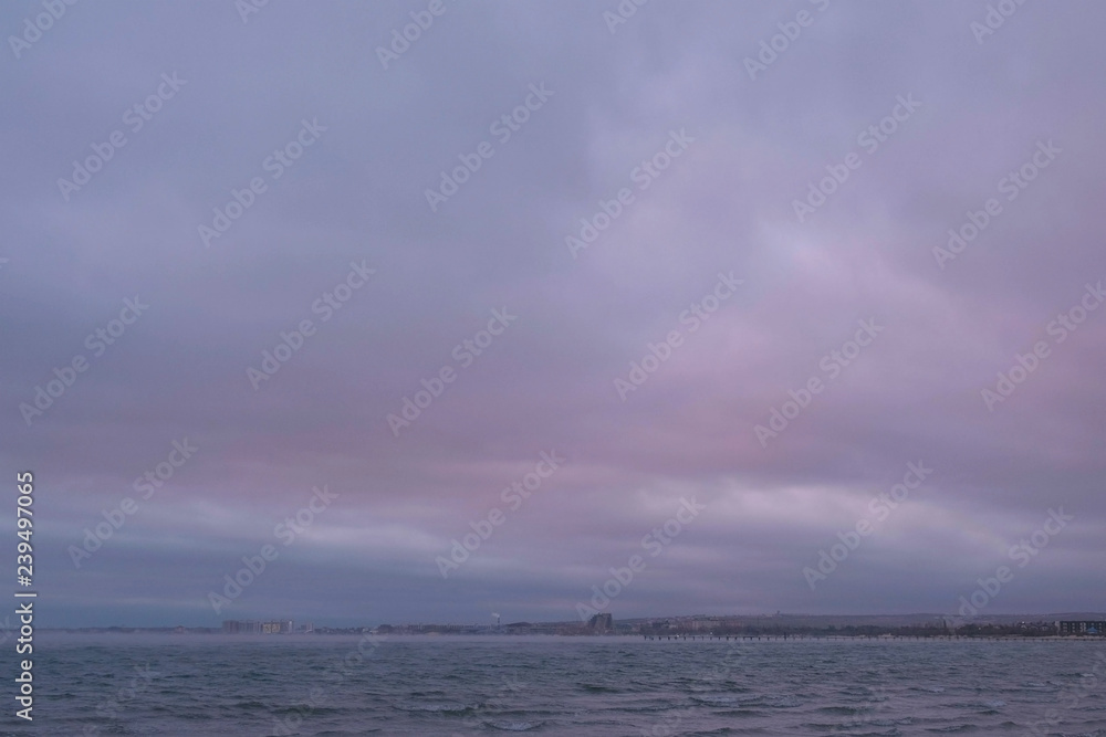 Mist and fog over the sea. Beautiful seascape with pink sunset and coastal town.