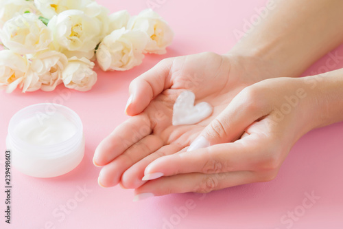 Young, perfect, clean woman's hands. Heart shape created from natural herbal cream. Love a body. Care about soft, smooth skin in summer time. Beautiful roses on pink table. Fresh flowers. 