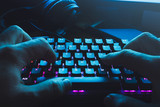 Male hands typing on the black illuminated  keyboard with blue light coming from screen