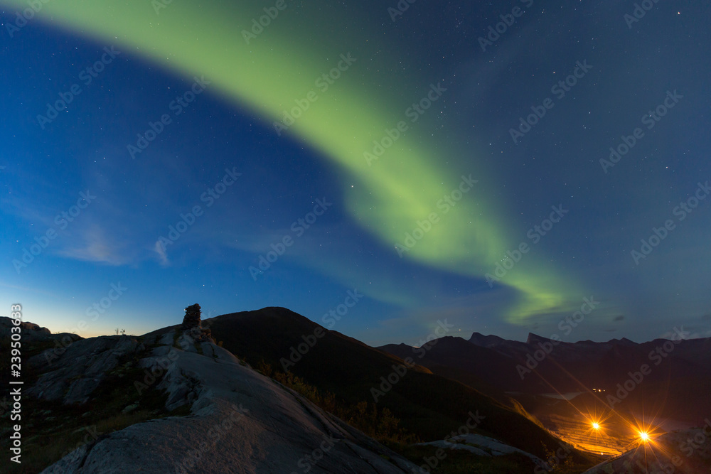 Northern lights dancing over mountain peaks with a silouette cairn in the front