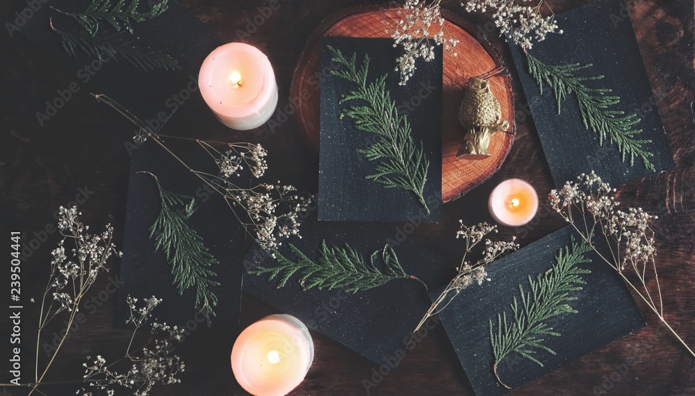 Flat lay home made diy festive black Yule (Christmas) cards with subtle  glitter sparkles and dried cedar branch glued on it. Natural decoration,  burning lit white candles, dried flowers in background Photos |