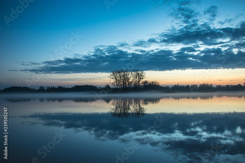 Evening fog on the shore of a calm lake.