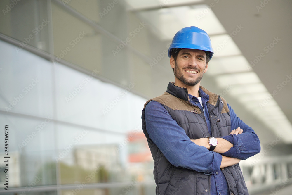 Smiling industrial worker in hardhat infront of modern building Smiling industrial worker in hardhat infront of modern building