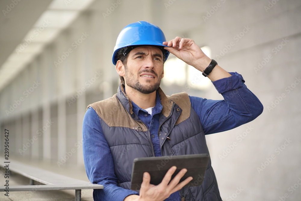 Attractive building expert in hardhat checking sight with tablet Attractive building expert in hardhat checking sight with tablet
