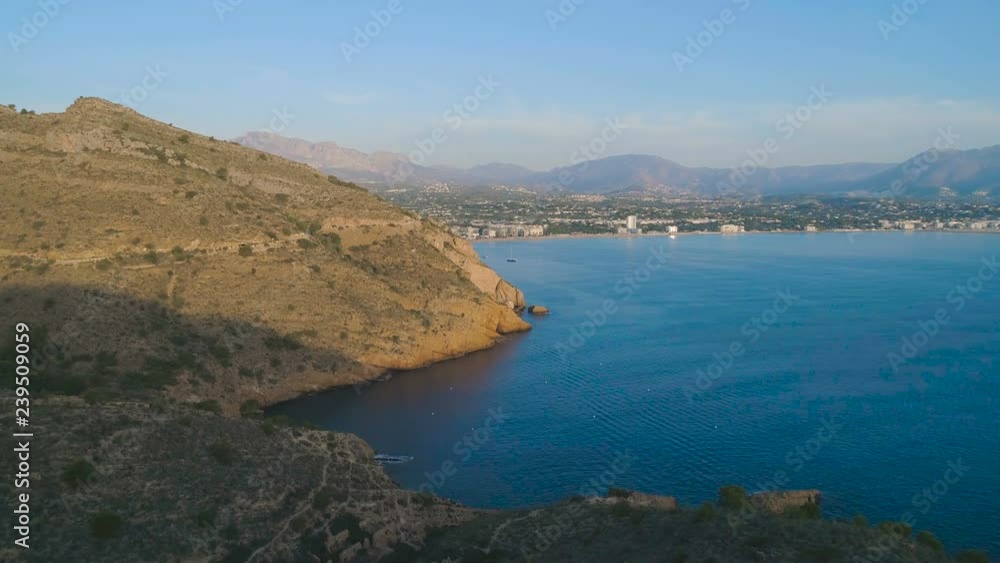 Aerial cinematic view, flying slow above blue sea along big yellow rocky mountain towards coastline, yachts and city view at sunset sunrise golden hour time. Beautiful summer autumn soft light Aerial cinematic view, flying slow above blue sea along big yellow rocky mountain towards coastline, yachts and city view at sunset sunrise golden hour time. Beautiful summer autumn soft light