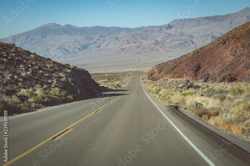 View from the endless road through Death Valley National Park (California State Route 190), with a view of the Sierra Nevada mountains in the background on a hazy sunny day © MelissaMN