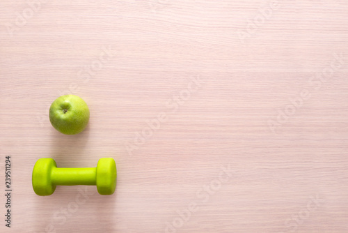 green dumbbell and green Apple on wooden Board background, top view