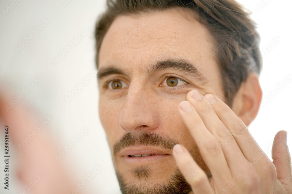 Obraz premium Handsome man checking wrinkles in mirror at home