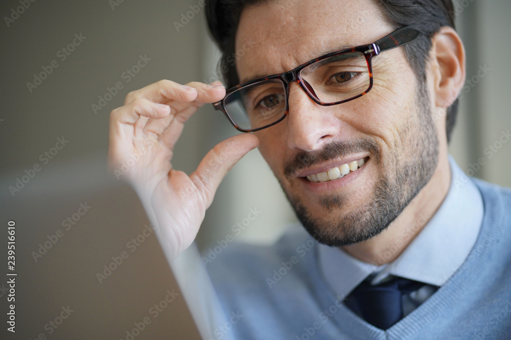 Portrait of attractive man smiling working on laptop wearing glasses Portrait of attractive man smiling working on laptop wearing glasses