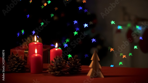 Burning candles with pines and wooden decorations standing on bright background
