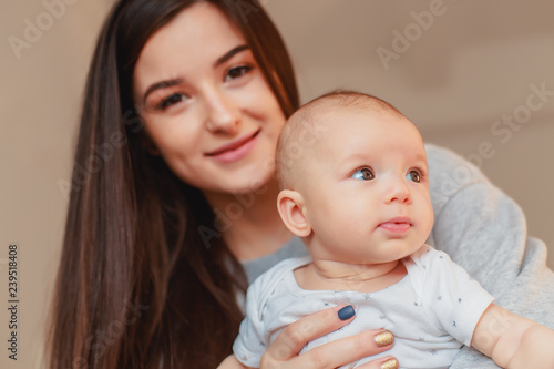 a beautiful young mother with dark hair and handsome eyes holds a baby with a beautiful face and model appearance