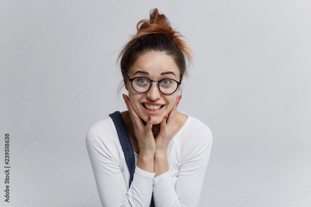 The girl see something nasty. She gritted her teeth. Pretty woman in white pullover and with top knot hairstyle looking at camera with shocked face and wide open eyes. The girl see something nasty. She gritted her teeth. Pretty woman in white pullover and with top knot hairstyle looking at camera with shocked face and wide open eyes.