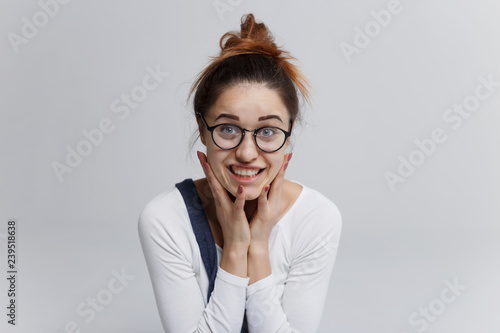 The girl see something nasty. She gritted her teeth. Pretty woman in white pullover and with top knot hairstyle looking at camera with shocked face and wide open eyes. 