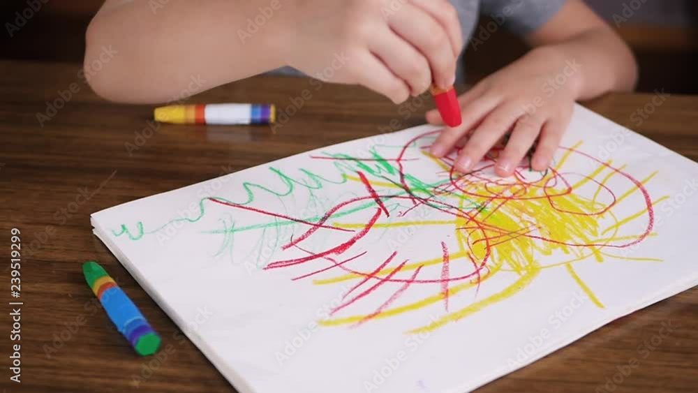 Close-up of the hands of a child, drawing on paper with bright color chalk or a pencil while sitting at the table. Creativity, the development of children of preschool age.