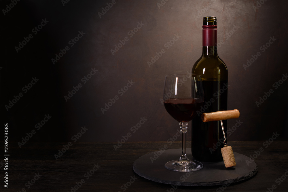 Fototapeta premium Wine bottle, glass with red wine and cork with corkscrew on dark wooden background. Celebration concept. Copy space