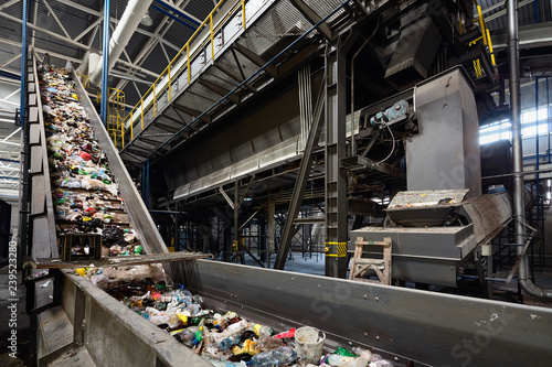 Conveyor belt at recycling plant transports garbage inside drum filter or rotating cylindrical sieve with trommel or screen for sorting pieces of garbage into various sizes fractions