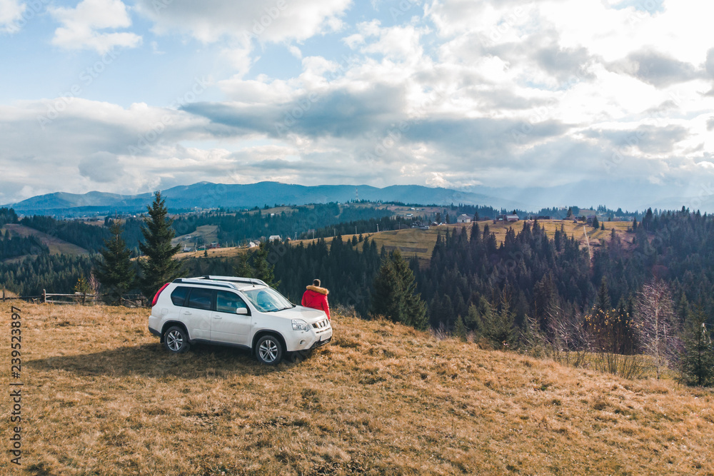man in red coat near white suv car at hill with beautiful mountains view man in red coat near white suv car at hill with beautiful mountains view