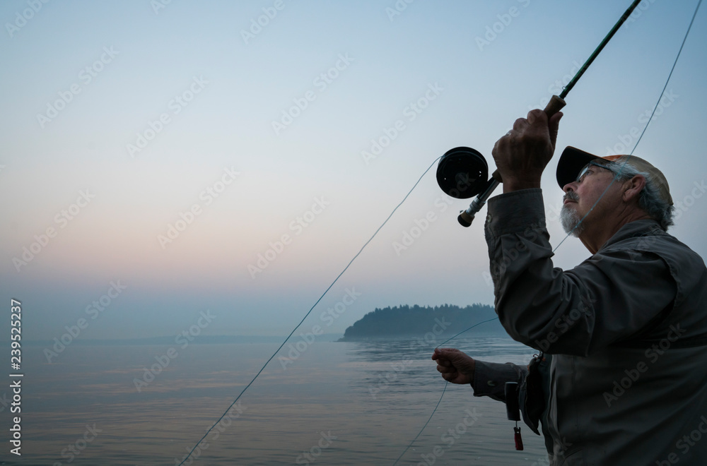 Senior Caucasian male fly fishing for salmon and sea run cutthroat trout in  Puget Sound near Port Orchard, Washington USA Stock Photo