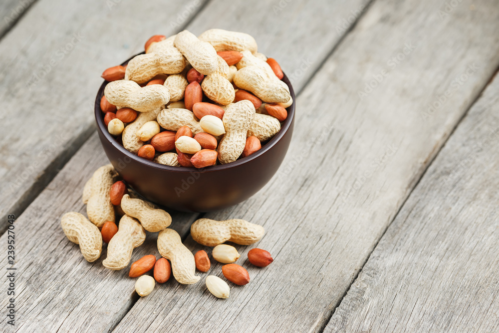 Roasted peanuts in the shell and peeled in a cup, against a gray wooden table Roasted peanuts in the shell and peeled in a cup, against a gray wooden table