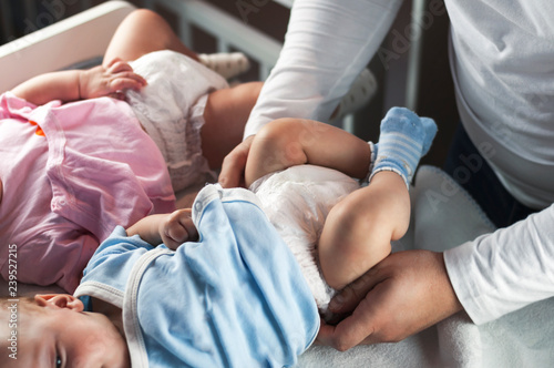 Young dad changes clothes and changes his diapers to his children, little twins, boy and girl. Selective focus.