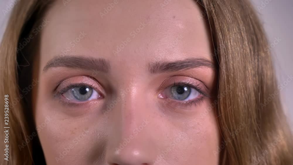 Close-up eye-portrait of blonde caucasian young woman watching directly into camera on gray background. Close-up eye-portrait of blonde caucasian young woman watching directly into camera on gray background.