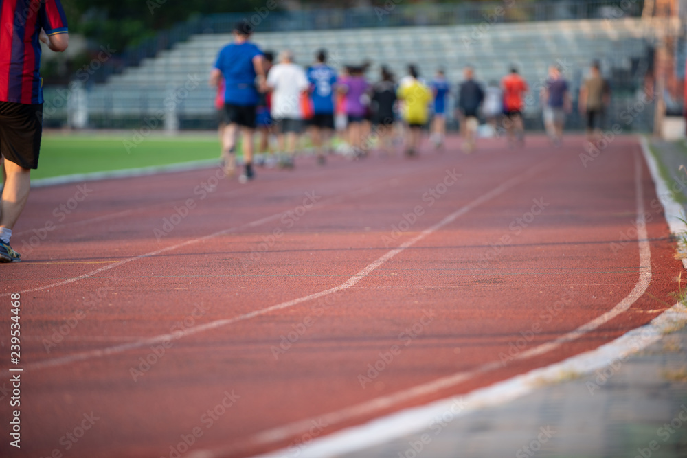 Groups of jogging people, with a variety of ages and sizes, running on the track in a stadium during the evening time with sun set. Groups of jogging people, with a variety of ages and sizes, running on the track in a stadium during the evening time with sun set.