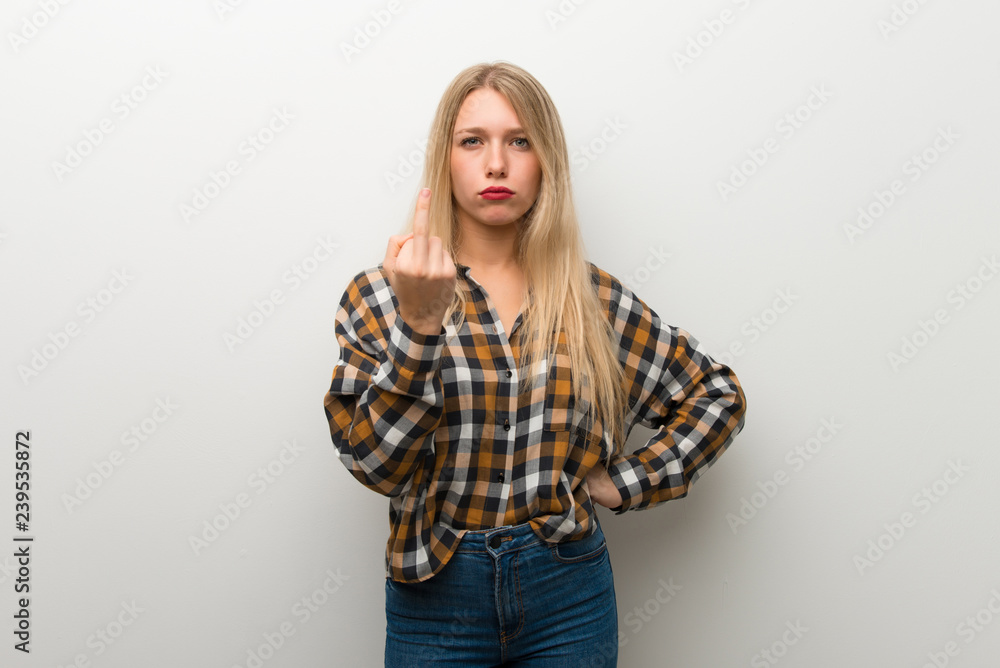 Blonde young girl over white wall making horn gesture Blonde young girl over white wall making horn gesture