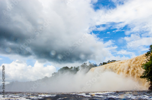 scenic landscape of venezuela canaima park with near majestic waterfalls and dramatic cloudy sky seen from boat in the river
