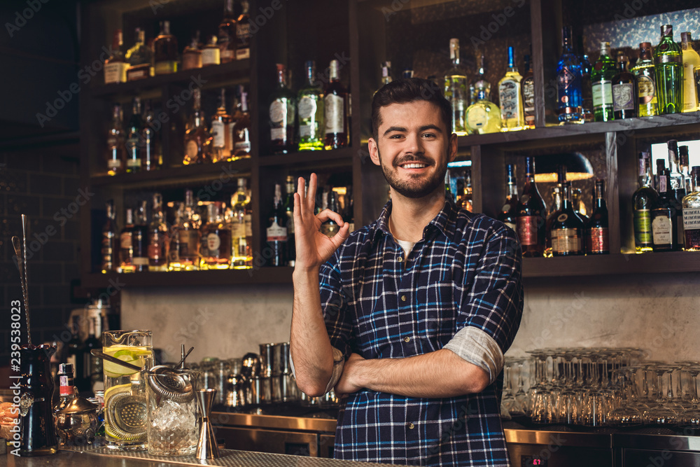 Young bartender standing at bar counter showing ok sign positive