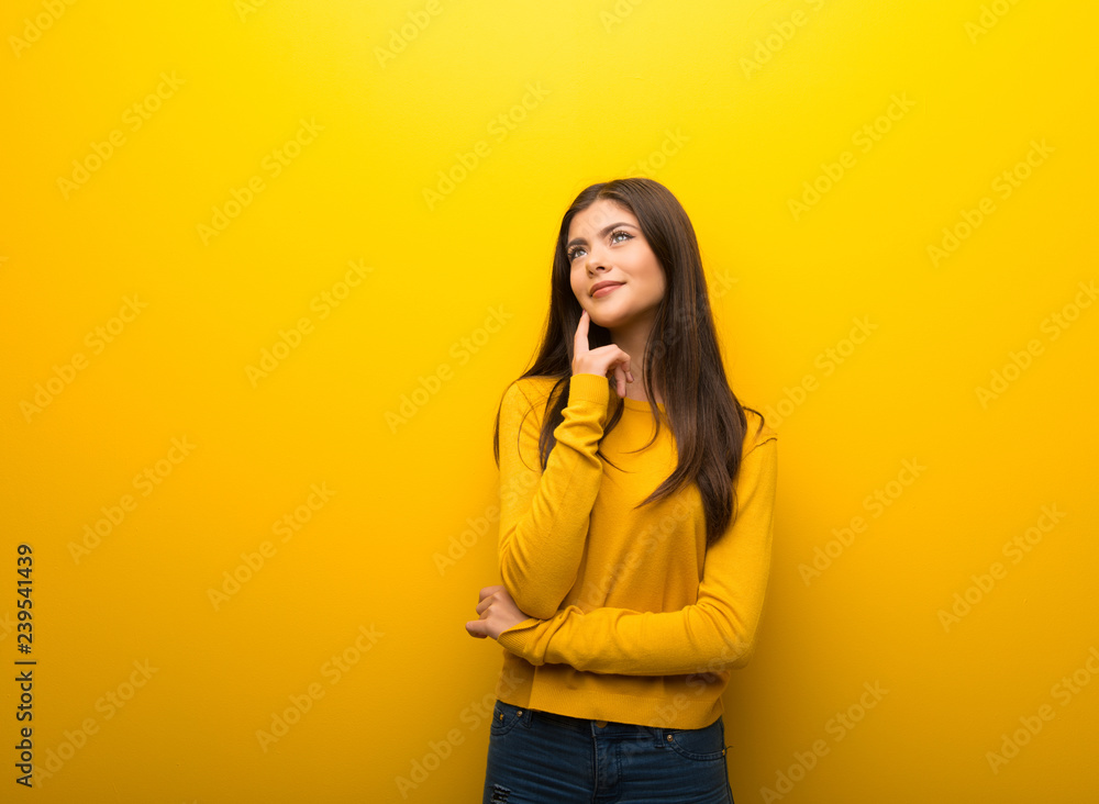 Teenager girl on vibrant yellow background thinking an idea while looking up Teenager girl on vibrant yellow background thinking an idea while looking up