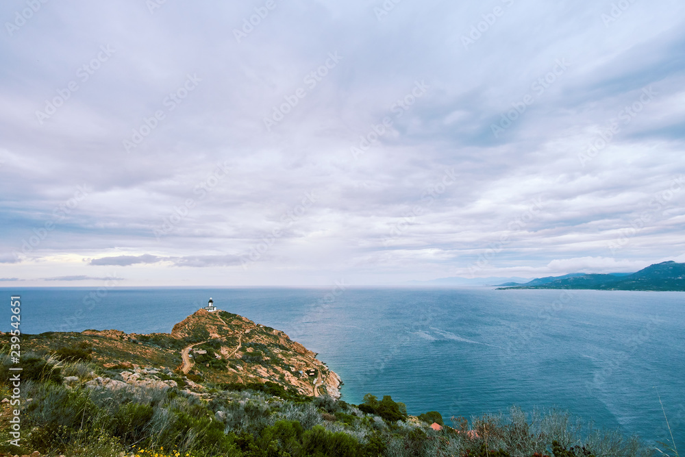 View of lighthouse in the distace on a cliff above the blue sea on cloudy day Corse, Corsica, France