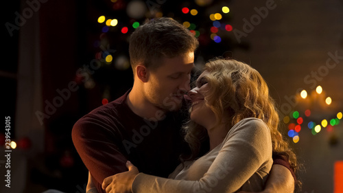 Loving couple embracing tenderly under Christmas tree, first holiday together